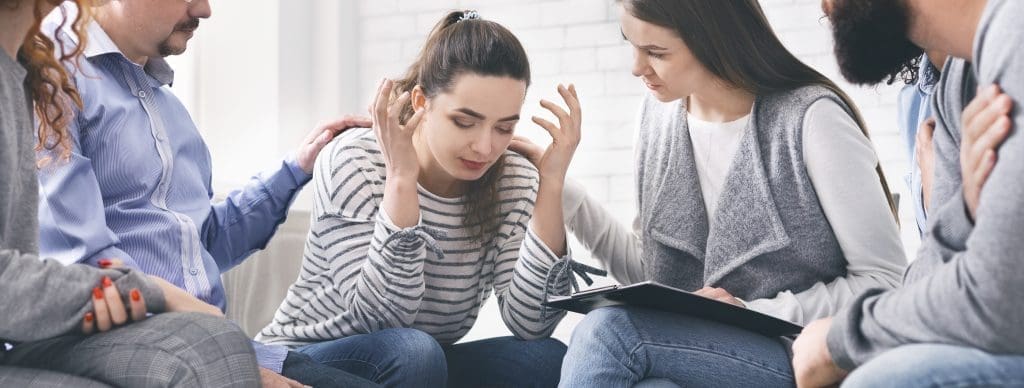 Group members supporting upset woman with drug addiction in rehab center