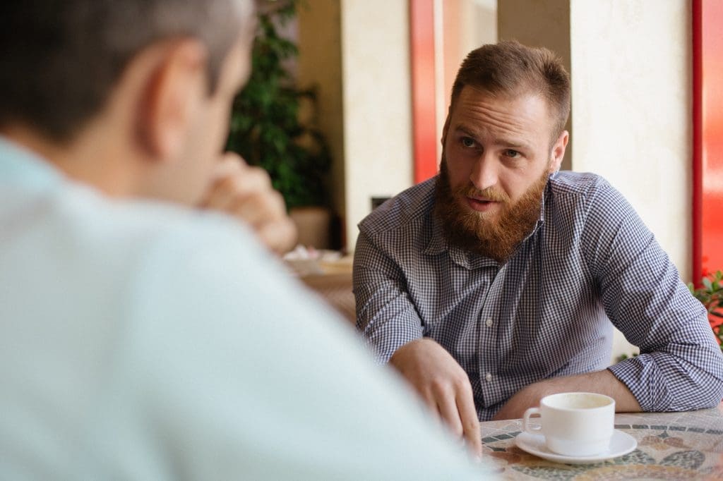 young man helping another over a coffee