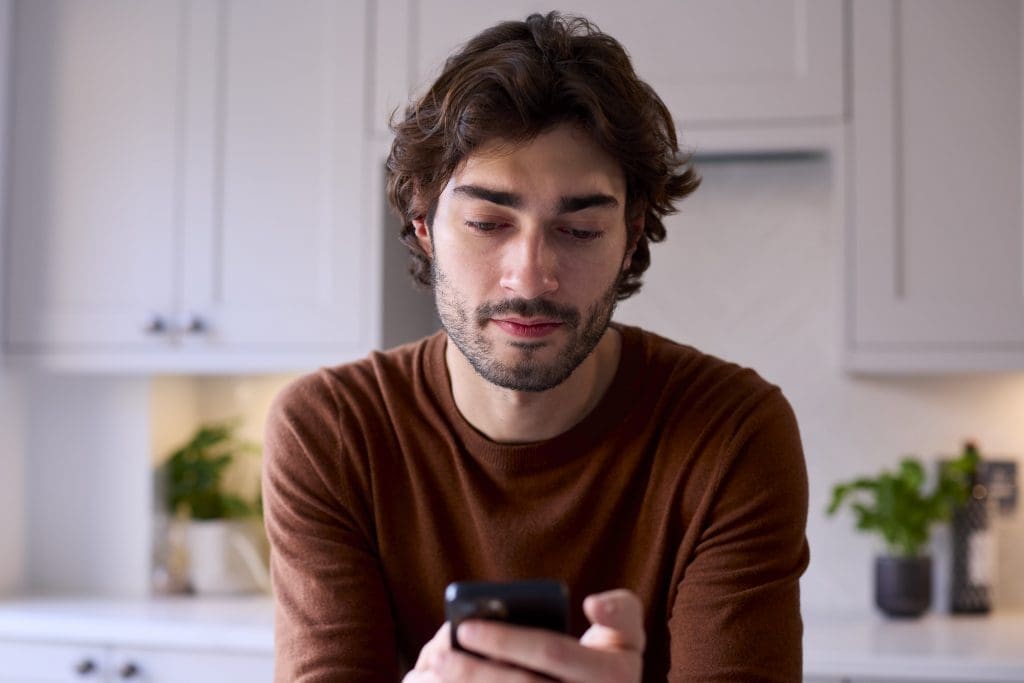 young-man-relaxing-at-home-in-kitchen-checking-mes-2024-10-21-23-18-45-utc-min