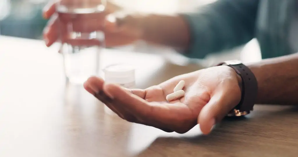 hand with two prescription drug pills, glass of water in background