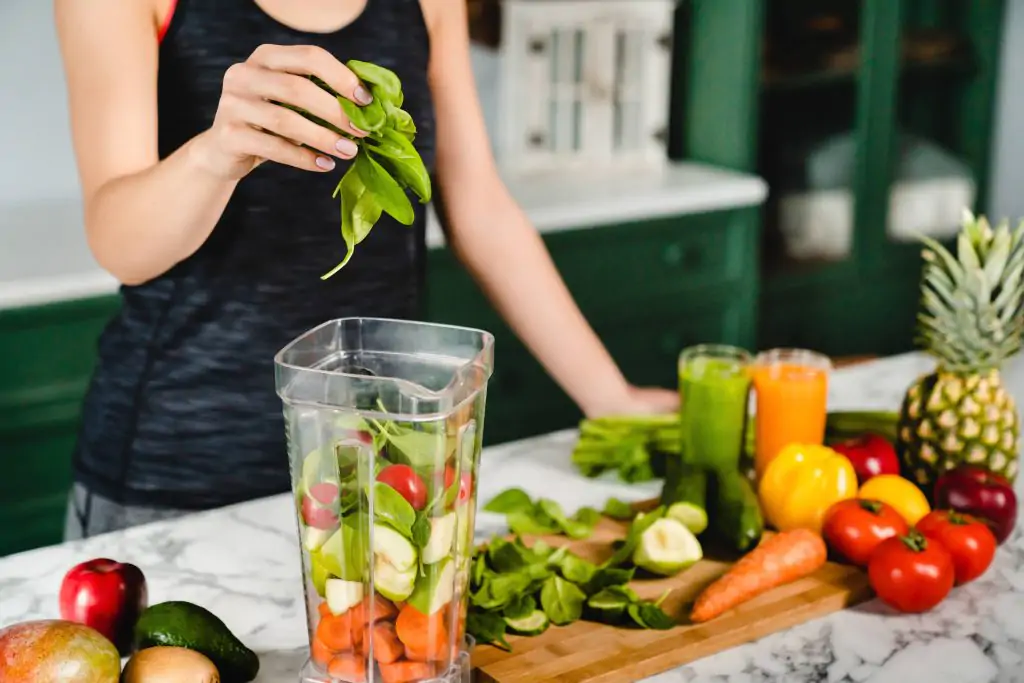 lady adding vegetables and fruit into a blender